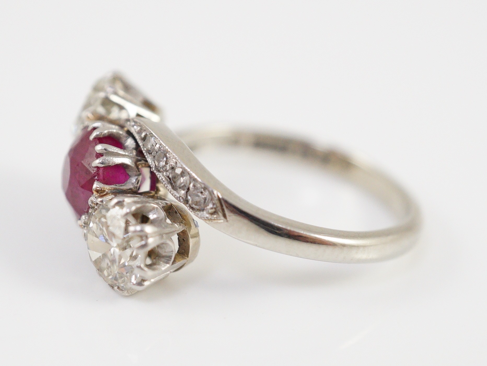 An 18ct white gold and platinum, two stone diamond and single stone synthetic? ruby set crossover ring, with diamond set shoulders